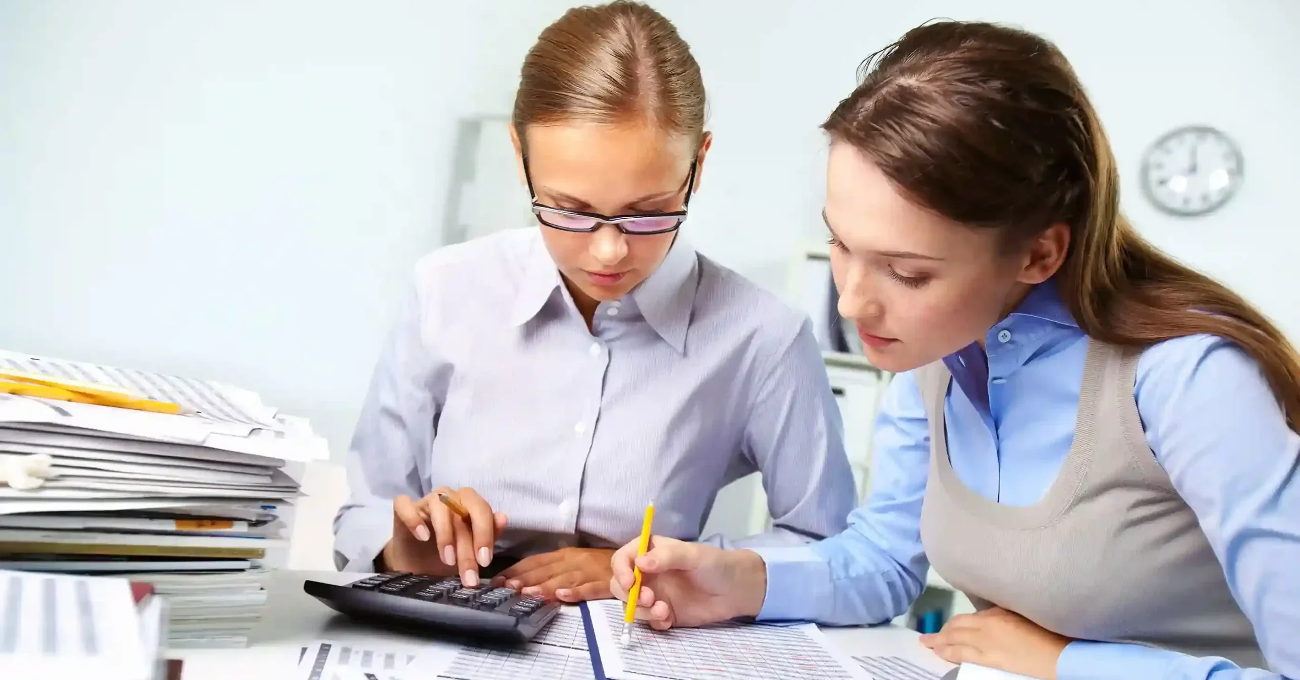 Two professional women working together at a desk, reviewing financial documents and using a calculator, representing accounting support for small businesses in the UK.